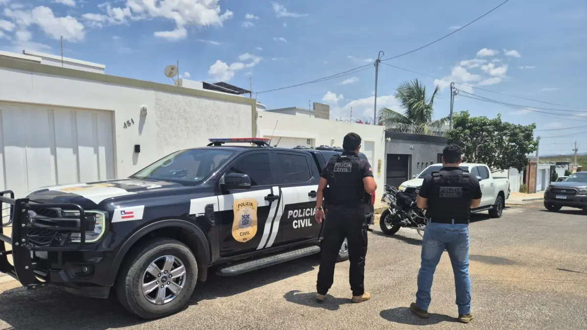 policiais civis ao lado de viatura da Polícia Civil e em frente de residência de investigado