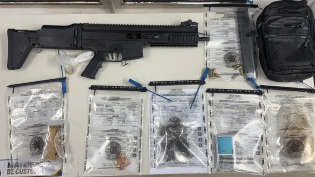 material apreendidos uma carabina calibre 9 mm, um carregador com 8 munições intactas, uma pedra grande de crack, 32 porções de maconha, um tablete de maconha prensada, 36 comprimidos de droga sintética, uma bolsa tiracolo e uma balança de precisão.