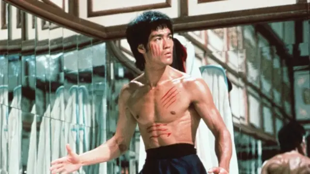 Bruce Lee em cena de filme de artes marciais, com expressão séria